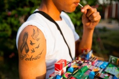 un ragazzo vende prodotti in strada mentre mangia un lecca lecca e mostra il suo tatuaggio sulla spalla